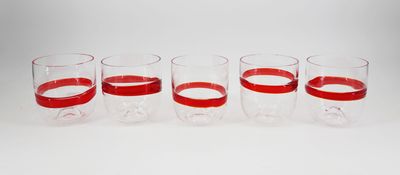 six verres aux bords rouges sont alignés sur une surface blanche
