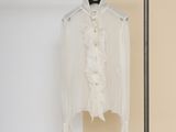 white shirt with ruffles hanging on a clothes rack in front of a beige wall