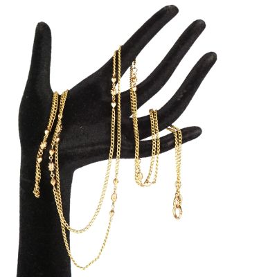 La main tient un bracelet en chaîne d'or et un gant noir.