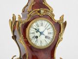 une horloge rouge et dorée posée sur une surface blanche