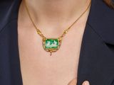 the woman is wearing a necklace with a green stone on it