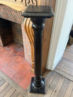 un socle noir placé devant une cheminée, sur lequel est posée une horloge