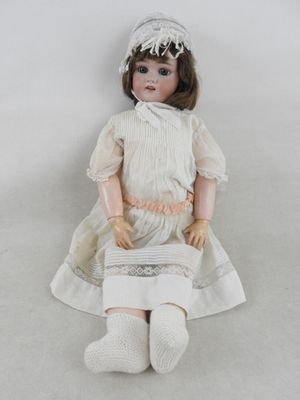 une poupée assise par terre, vêtue d'une robe blanche et d'un chapeau
