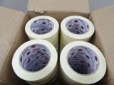 four rolls of tape are in a cardboard box on the floor