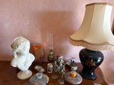 a table with a lamp, a bust, a candle, a candle holder, and other items on it