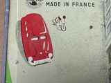 une petite boîte en fer-blanc sur laquelle est représentée une voiture rouge