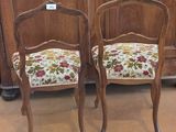 pair of antique chairs with floral upholstered cushions in front of a wooden cabinet