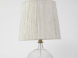 La lampe est en verre et est munie d'un abat-jour blanc.