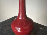 un vase rouge avec une anse dorée posé sur une table noire