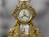 a gold clock sitting on top of a table next to a candle