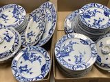 Des boîtes contenant des assiettes en porcelaine bleues et blanches sont empilées les unes sur les autres