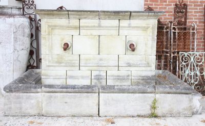a stone water fountain sitting in front of a brick building