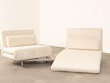 pair of white lounge chairs in a white room with concrete flooring