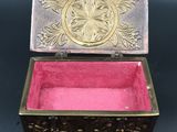an ornate brass box with pink velvet lining on a black surface