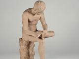 statue of a man sitting on a rock with his legs crossed