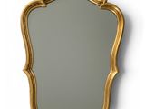 un miroir à cadre doré accroché au mur, à côté d'un mur blanc