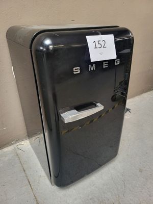 a small black refrigerator sitting on the sidewalk next to a wall