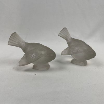 une paire de figurines d'oiseaux en verre posées sur une surface blanche