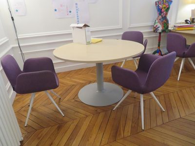 des chaises violettes disposées autour d'une table ronde dans une pièce aux murs blancs