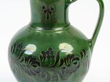 a green vase with a black handle sitting on a white surface