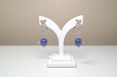 des boucles d'oreilles ornées de perles de verre bleues, posées sur un support blanc sur une table
