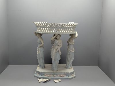 une statue représentant trois femmes tenant un panier posé sur une table