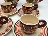 several cups and saucers are sitting on a table with a teapot in the background