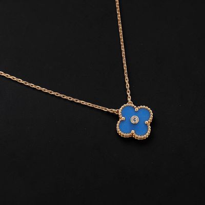 a gold necklace with a blue flower pendant on a black background