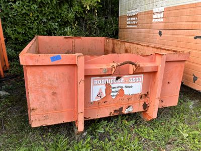 a red dumpster sitting in the grass next to a building