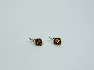 une paire de petites boucles d'oreilles en or posées sur une surface blanche