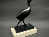 statue d'un oiseau noir posée sur un socle en marbre, sur fond gris