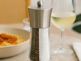 un moulin à poivre en argent et un verre de vin posés sur une table