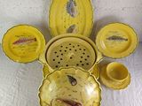 a yellow plate with a fish design on it next to other dishes and cups