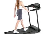 La femme marche sur un tapis roulant, un téléphone à la main.