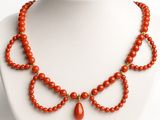 an orange beaded necklace with a tear shaped pendant on a white mannequin