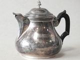 a silver tea pot with a black handle on a table