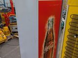 a coca cola machine in a warehouse with other machines in the background