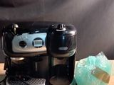 a black coffee maker on a wooden table next to a cup