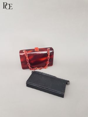 un sac à main rouge et une boîte noire posés sur une surface blanche