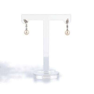 une paire de boucles d'oreilles en perles et diamants, présentée sur un présentoir transparent