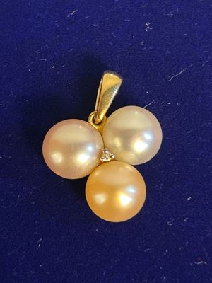a close up of a yellow pearl and diamond pendant on a blue surface
