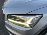 the front end of a silver car with its headlights turned on