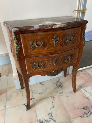 a small wooden chest of drawers on a marble floor