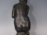 a statue of a woman sitting on a rock with her back to the camera