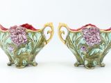 pair of green and pink vases with flowers on them on a white surface