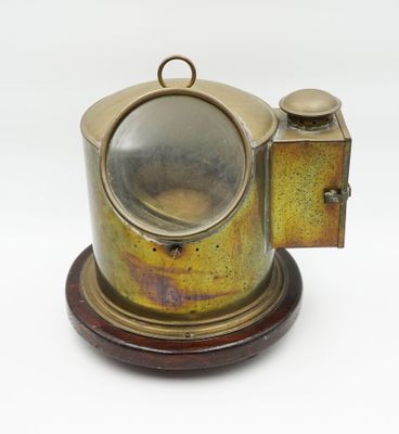 une théière ancienne en laiton reposant sur un socle en bois, sur fond blanc