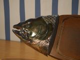 a metal fish head on a wooden plaque on a table