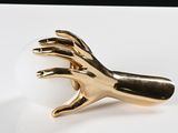 a gold hand holding a white ball on a white plate