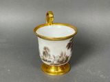 a small cup with a gold handle on a gray surface