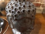 sculpture représentant une tête percée de trous, posée sur une table à côté d'une lampe